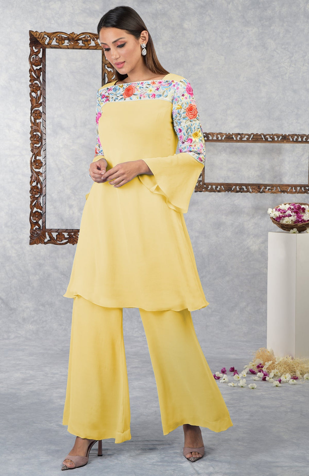 A woman models a yellow Parsi Gara embroidered kurta set with bell sleeves.