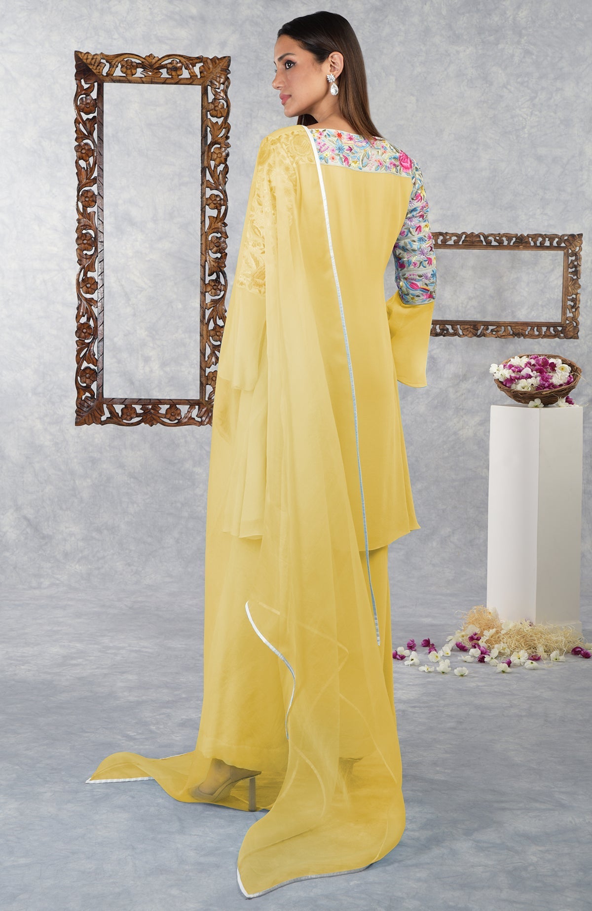 A woman models a yellow Parsi Gara embroidered kurta set with a floral neckline.