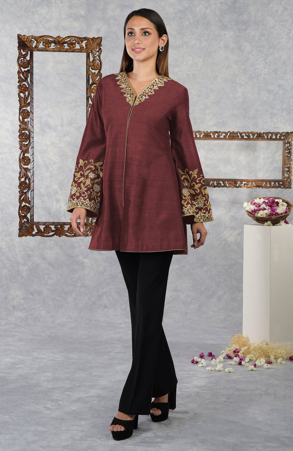 A woman models a pomegranate raw silk hand-embroidered jacket with black pants and platform heels.