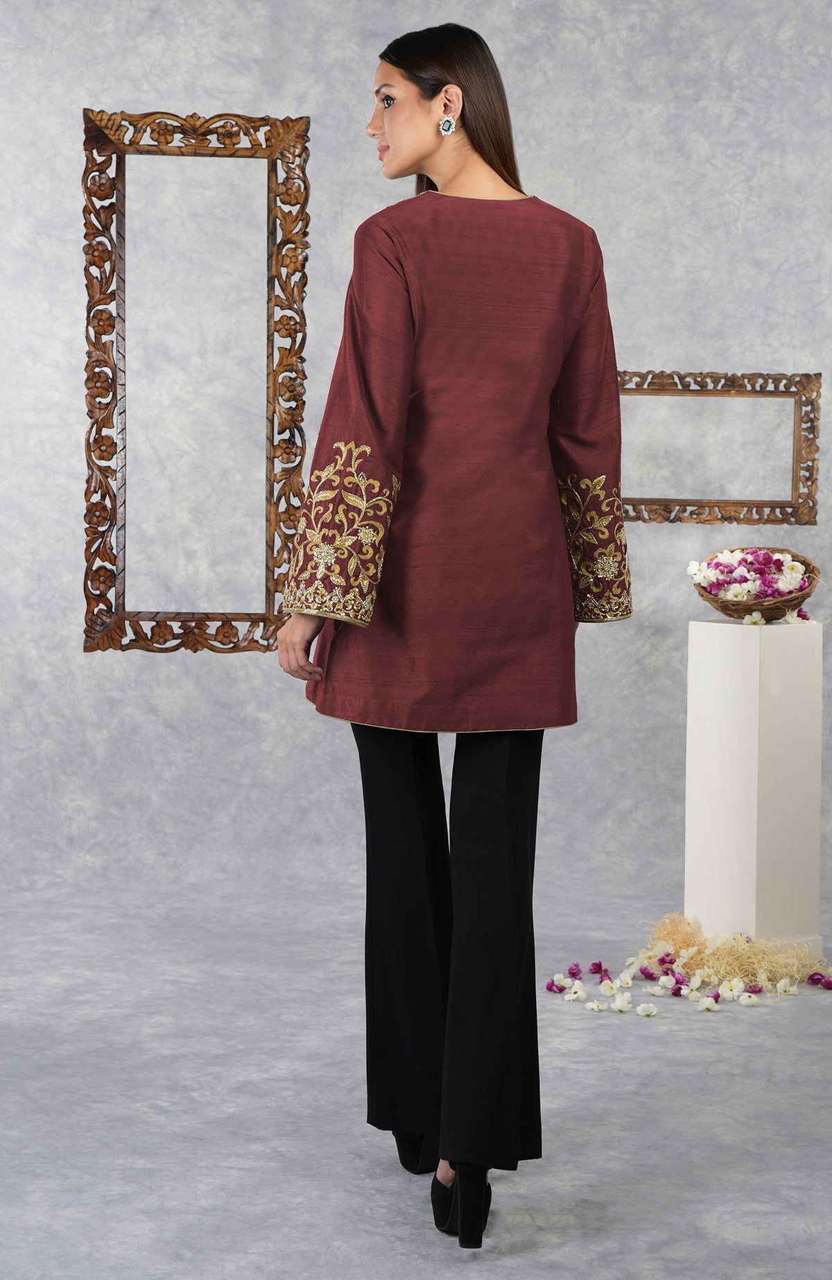 A woman models a pomegranate raw silk hand-embroidered jacket with black pants.