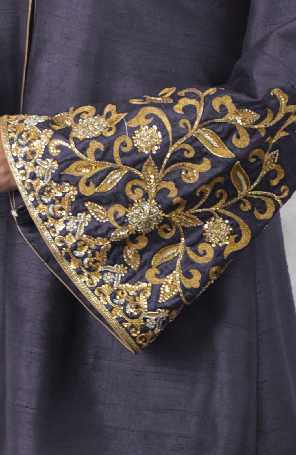 A close-up of a smoky violet raw silk jacket sleeve with gold embroidery.