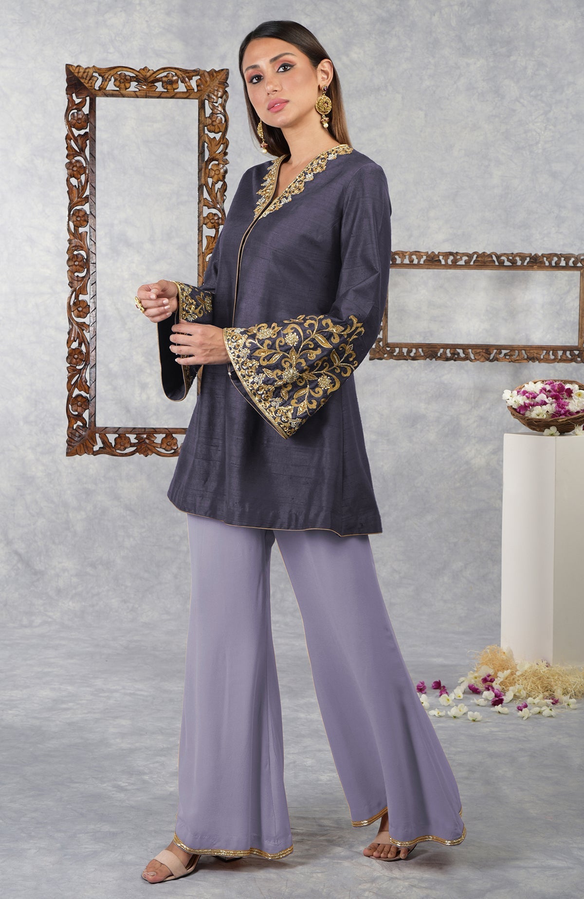 A woman models a smoky violet raw silk hand-embroidered jacket set with pastel lilac palazzo pants.