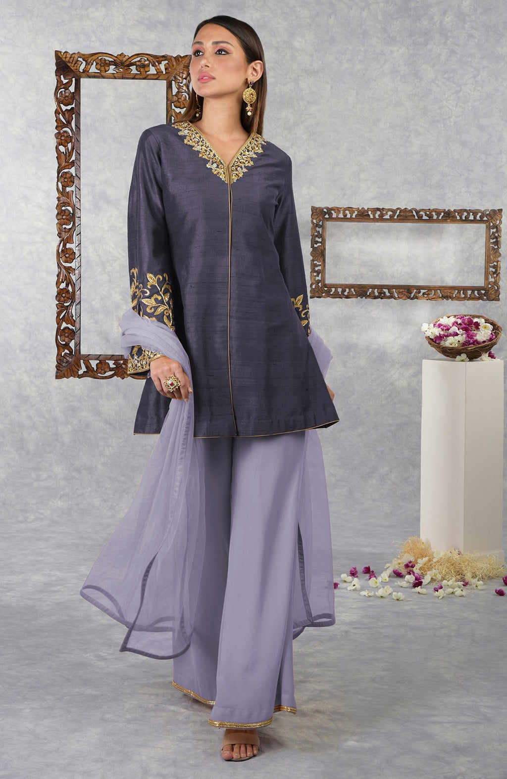 A woman models a smoky violet raw silk jacket set with pastel lilac palazzo pants and dupatta.