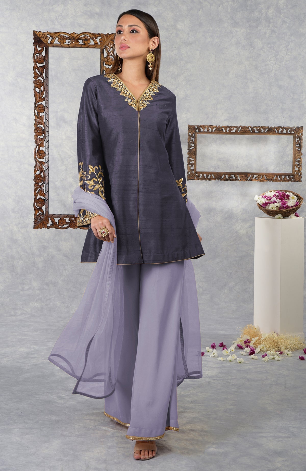 A woman models a smoky violet raw silk jacket set with pastel lilac palazzo pants and dupatta.