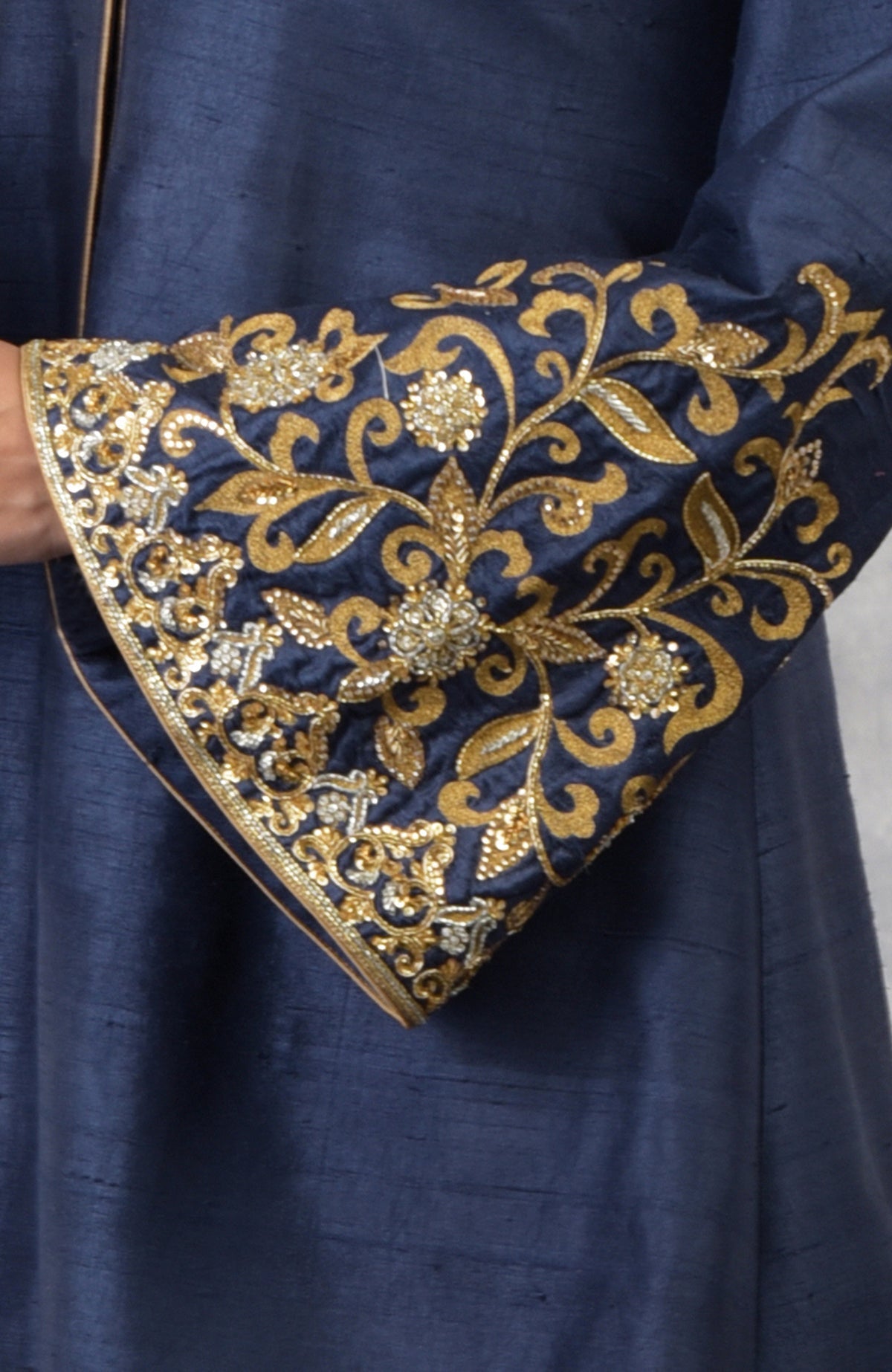 A close-up of a navy blue raw silk jacket with intricate gold embroidery on the sleeve.