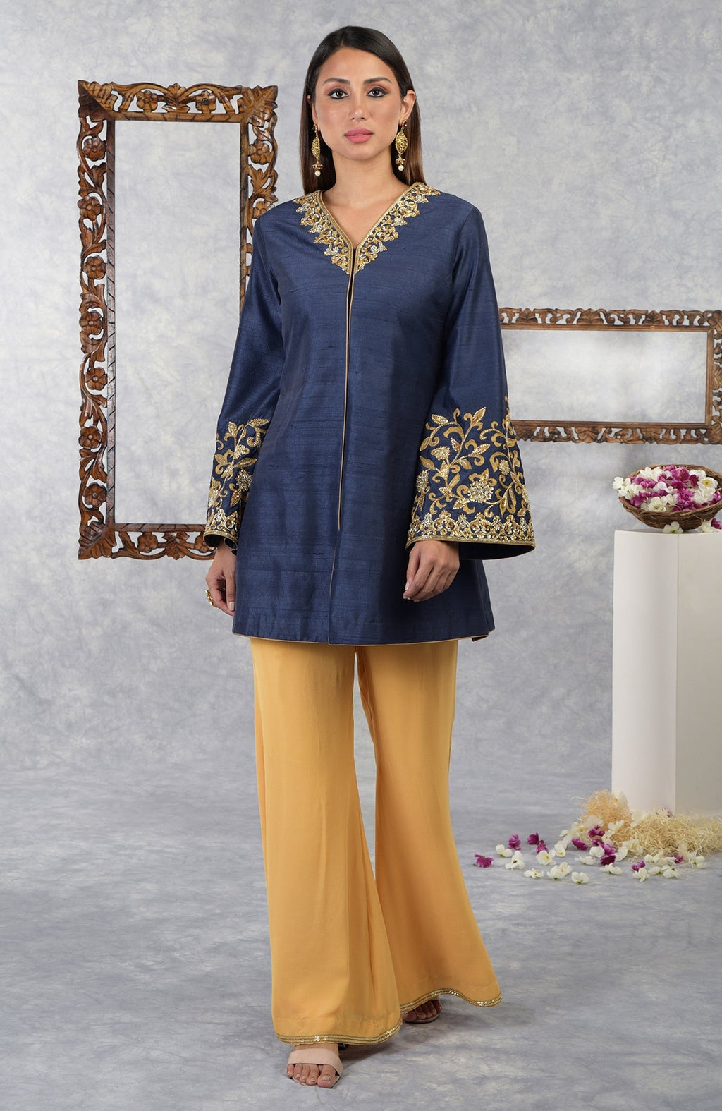 A woman models a navy blue raw silk jacket with gold embroidery and honey yellow palazzo pants.
