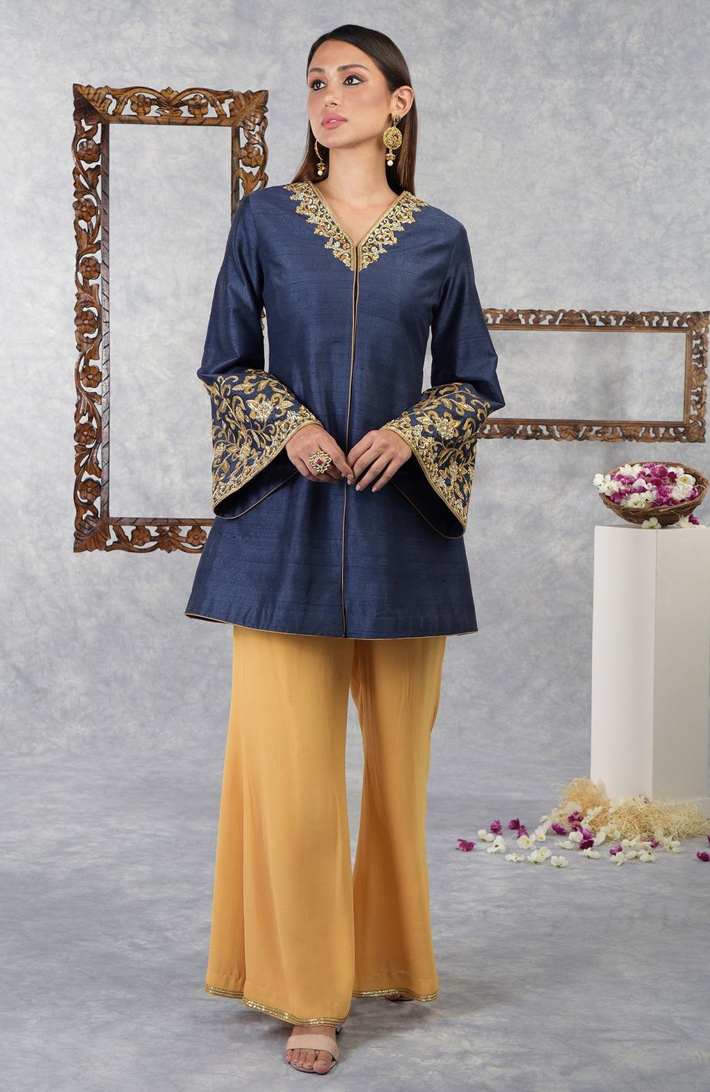 A woman models a navy blue raw silk jacket with gold embroidery and honey yellow palazzo pants.