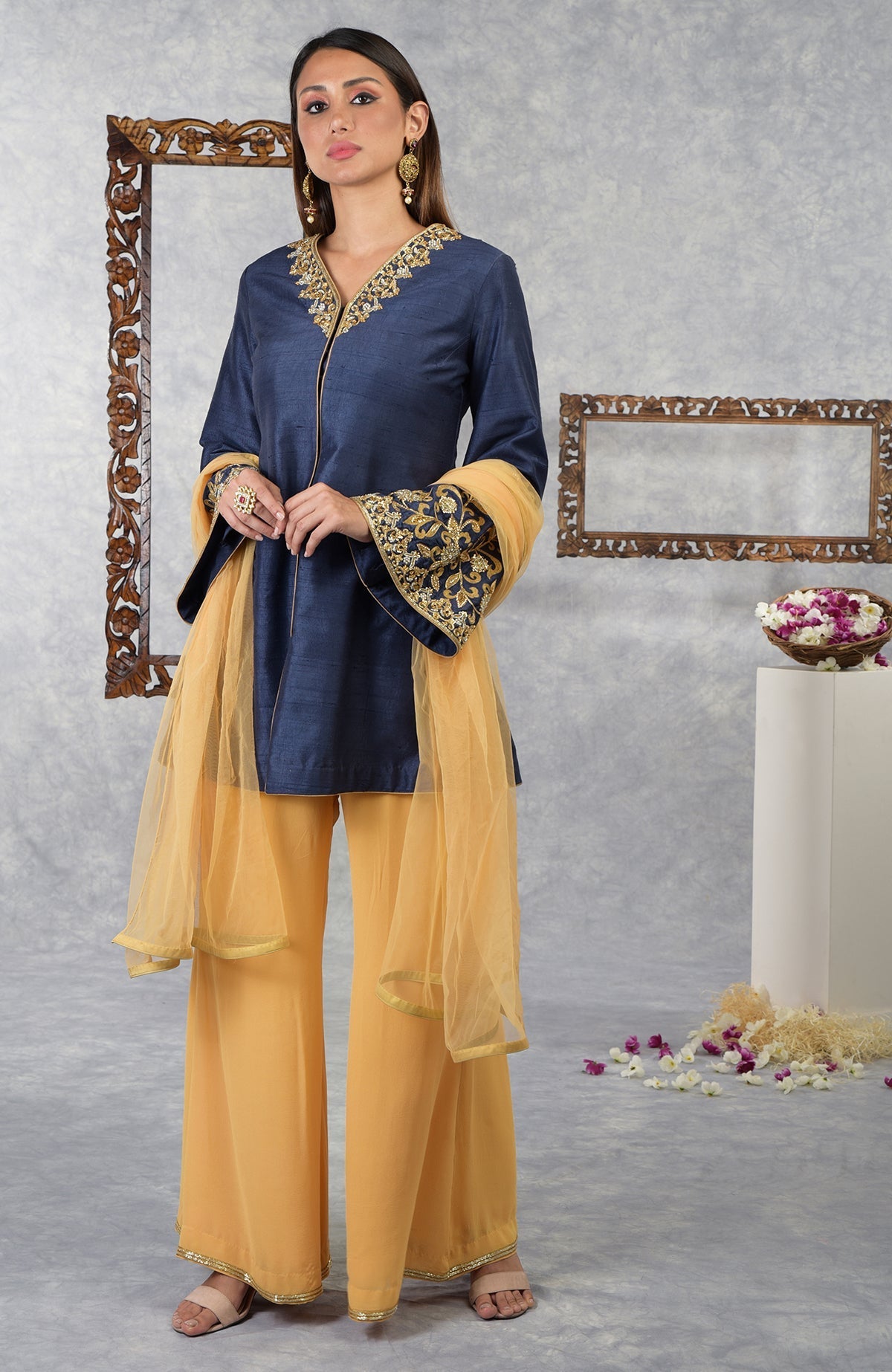A woman models a navy blue raw silk jacket set with honey yellow palazzo pants and dupatta.