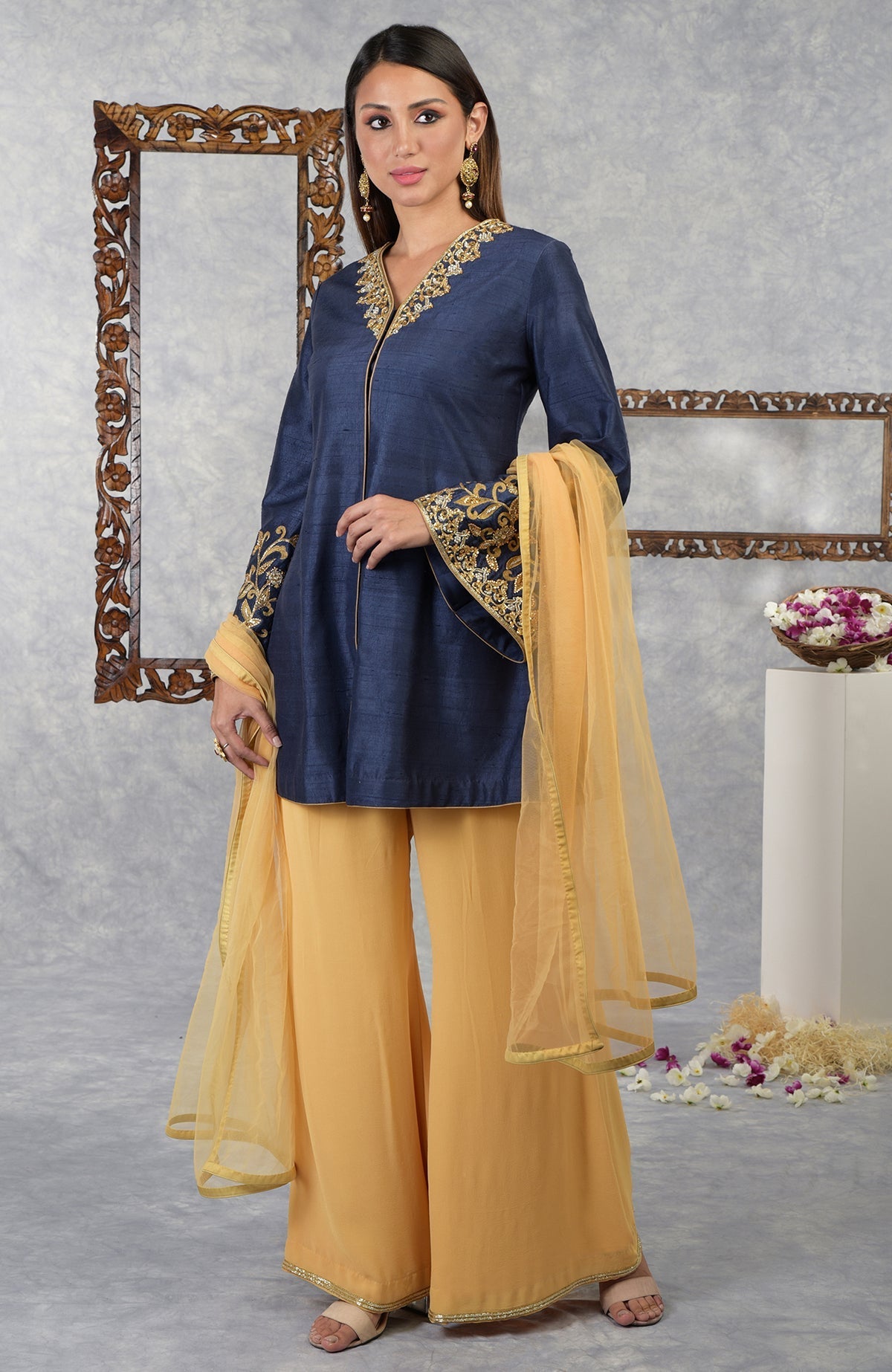A woman models a navy blue raw silk jacket set with honey yellow palazzo pants and dupatta.