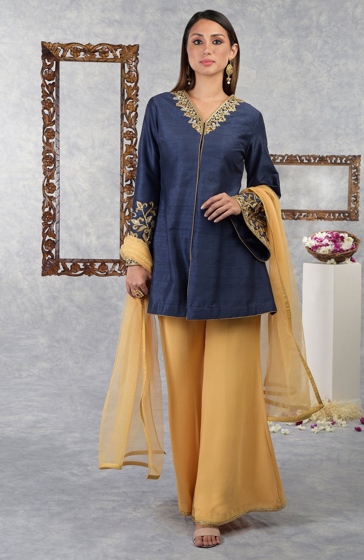 A woman models a navy blue raw silk jacket set with honey yellow palazzo pants and dupatta.