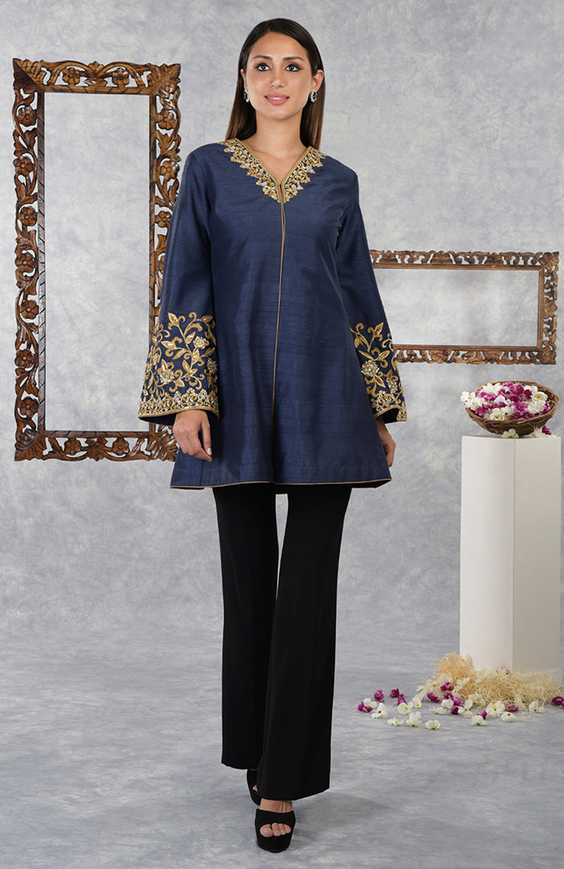 A woman models a navy blue raw silk jacket with gold embroidery and black flared pants.