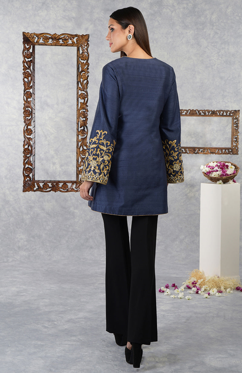 A woman models a navy blue raw silk jacket with gold embroidery and black flared pants.