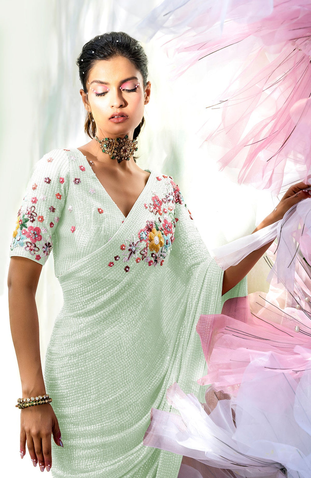 A woman models a sage green floral sequin saree with a matching blouse.
