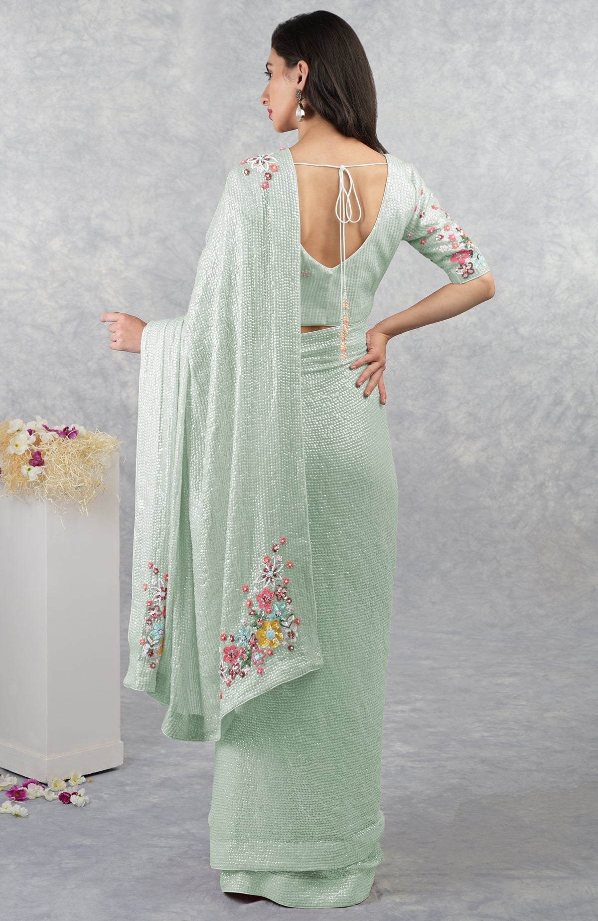 A woman models a sage green floral sequin saree with an open back blouse.