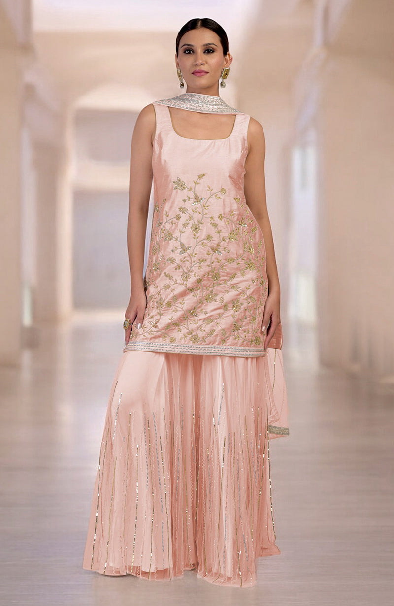 A woman models a light pink embroidered sharara set with a matching dupatta.