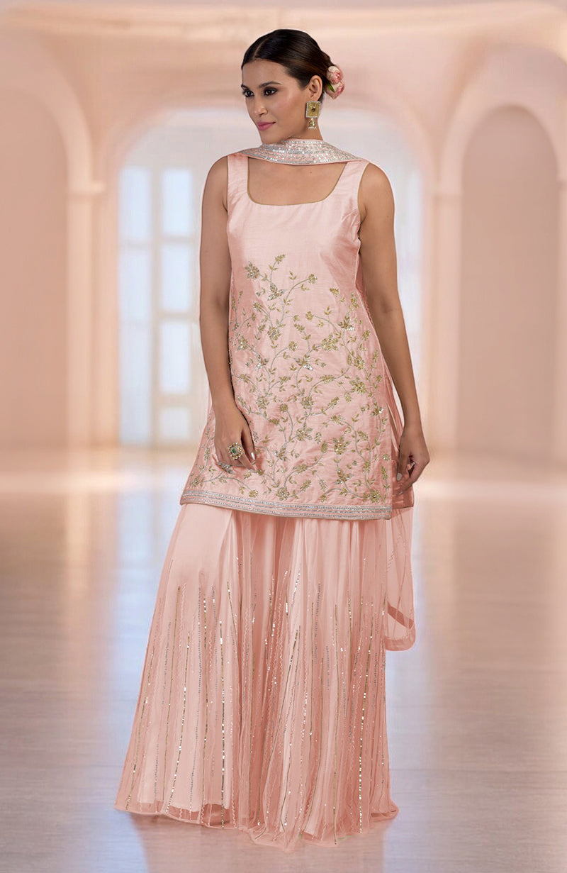 A woman models a rose gold hand-embroidered sharara set with a sleeveless kurta.
