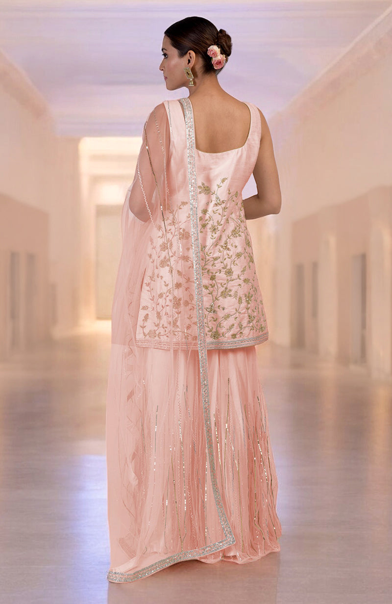 A woman models a rose gold hand-embroidered sharara set with a matching dupatta.