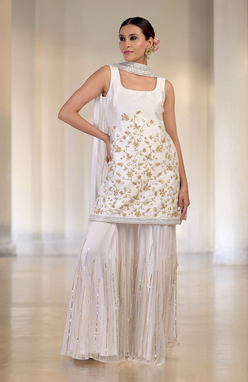 A model wears a white and gold hand-embroidered sharara set with a matching dupatta.