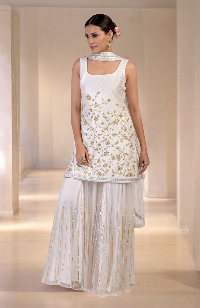A woman models a white and gold embroidered sharara set with a matching dupatta.