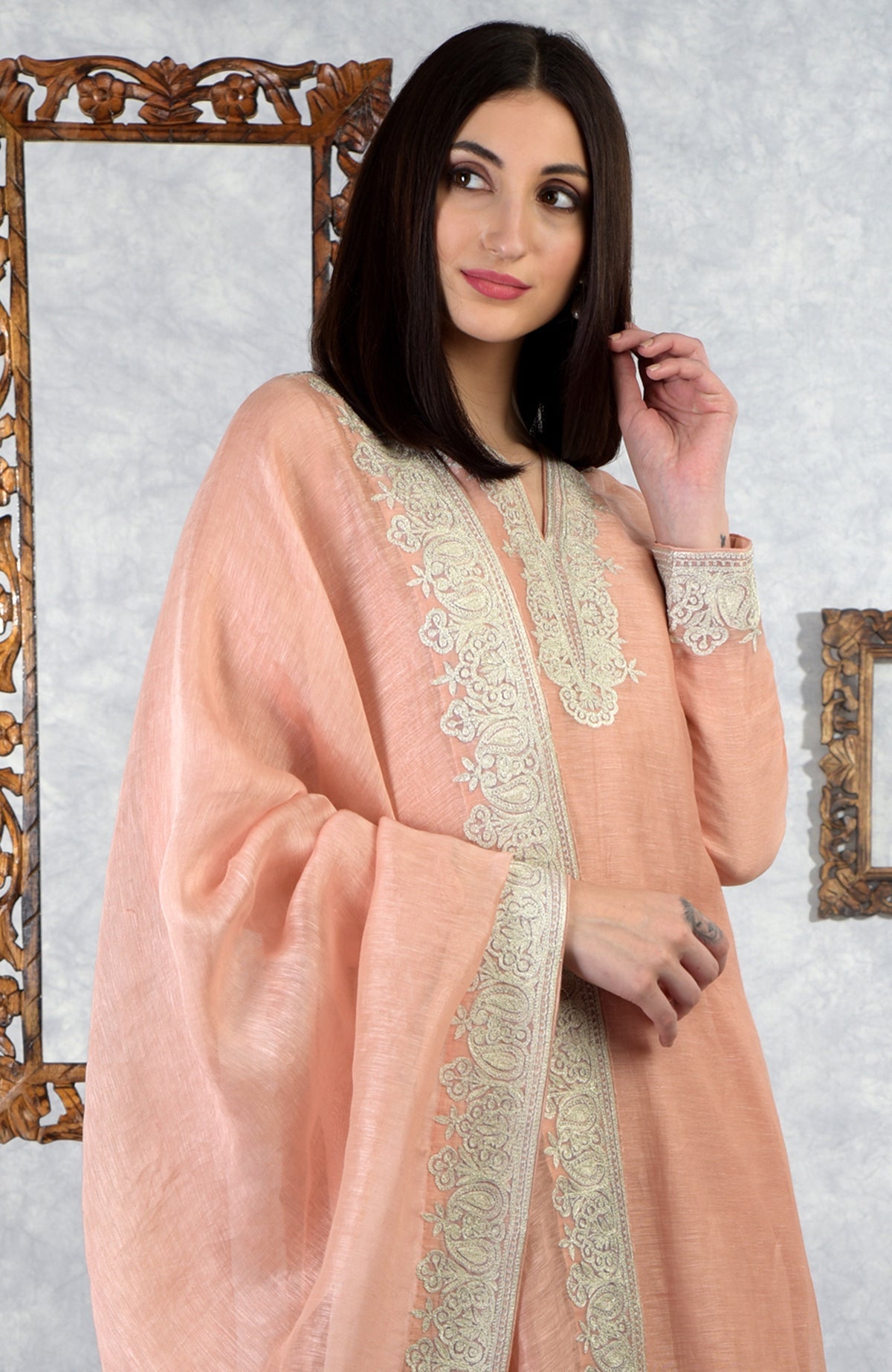 A woman models a pale peach Kashmiri Tilla embroidered kurta set.