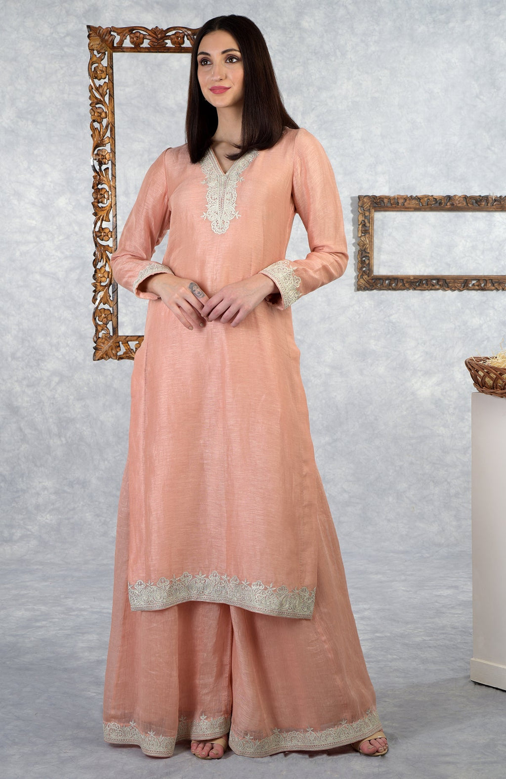 A woman models a pale peach Kashmiri Tilla embroidered kurta set with a sharara.