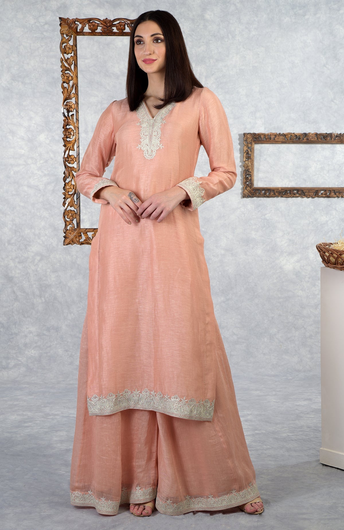 A woman models a pale peach Kashmiri Tilla embroidered kurta set with a sharara.