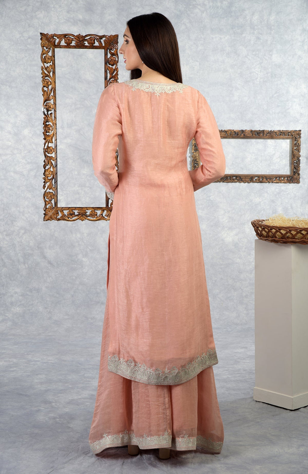 A woman models a pale peach Kashmiri Tilla embroidered kurta set from the back.