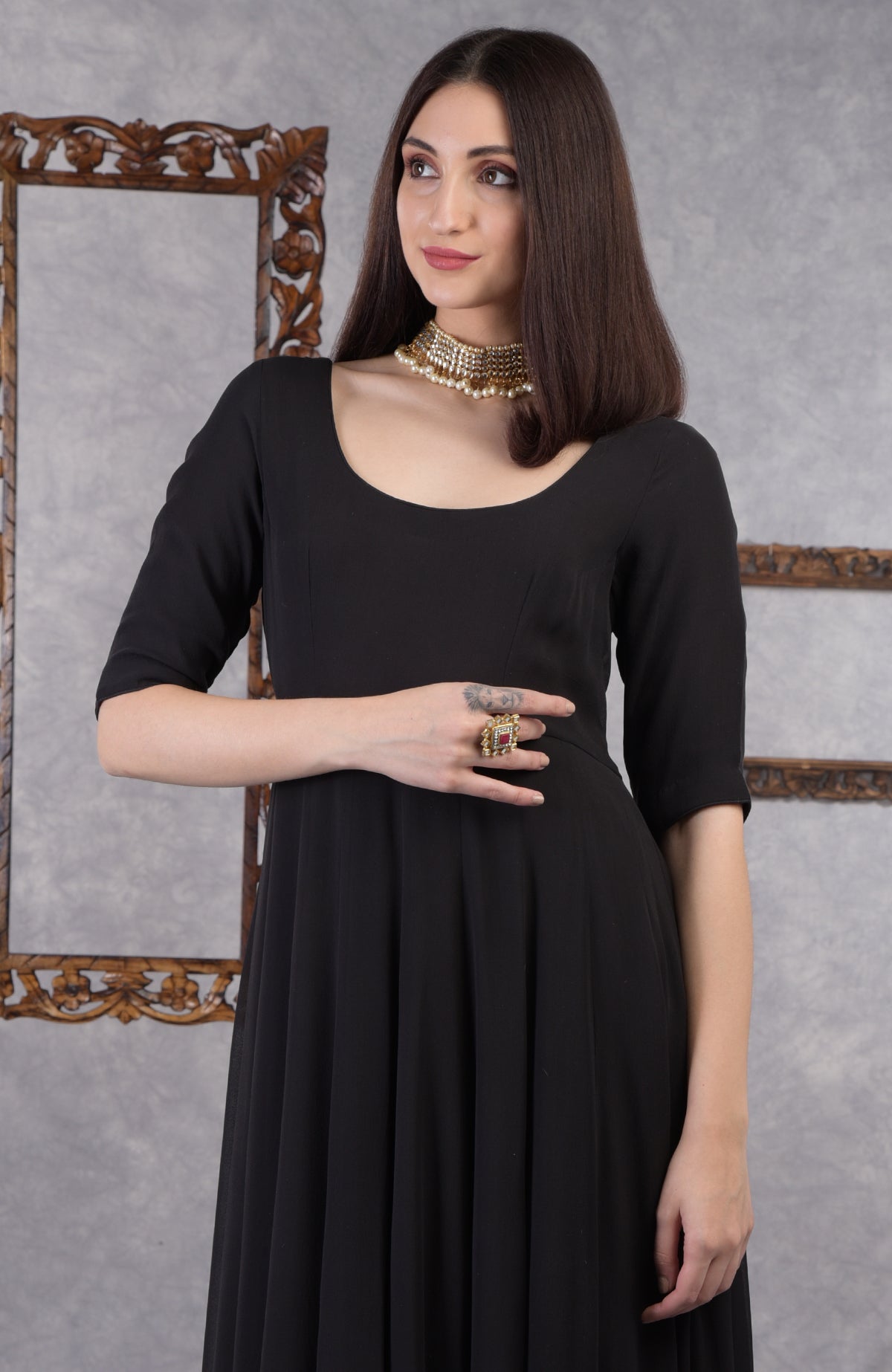 A woman in a black pure georgette Anarkali set with a gold choker and ring.