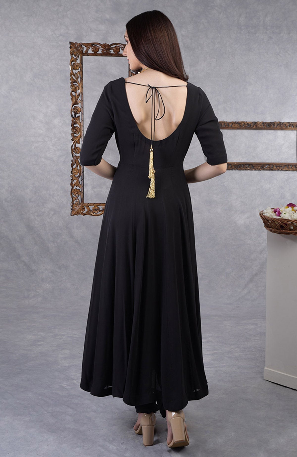 A woman from behind wears a black georgette anarkali with a deep back and gold tassel.