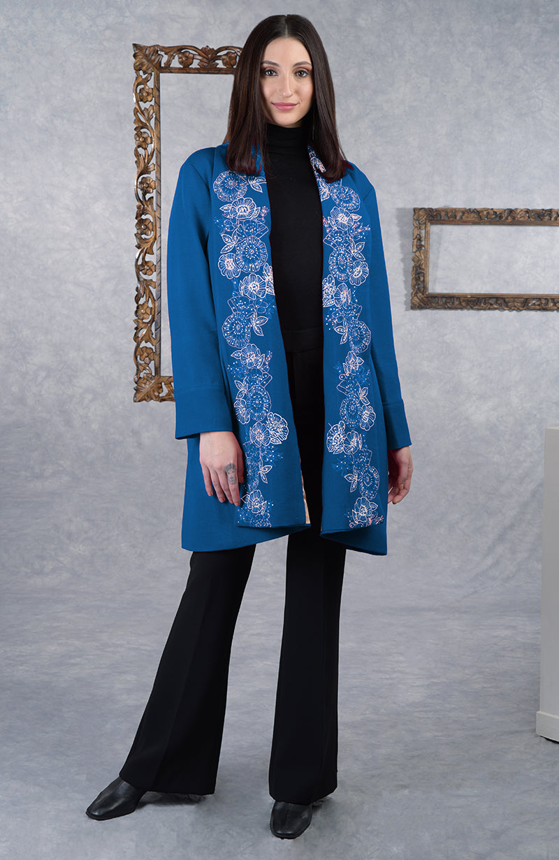 A woman models a blue wool crepe jacket with white floral embroidery.