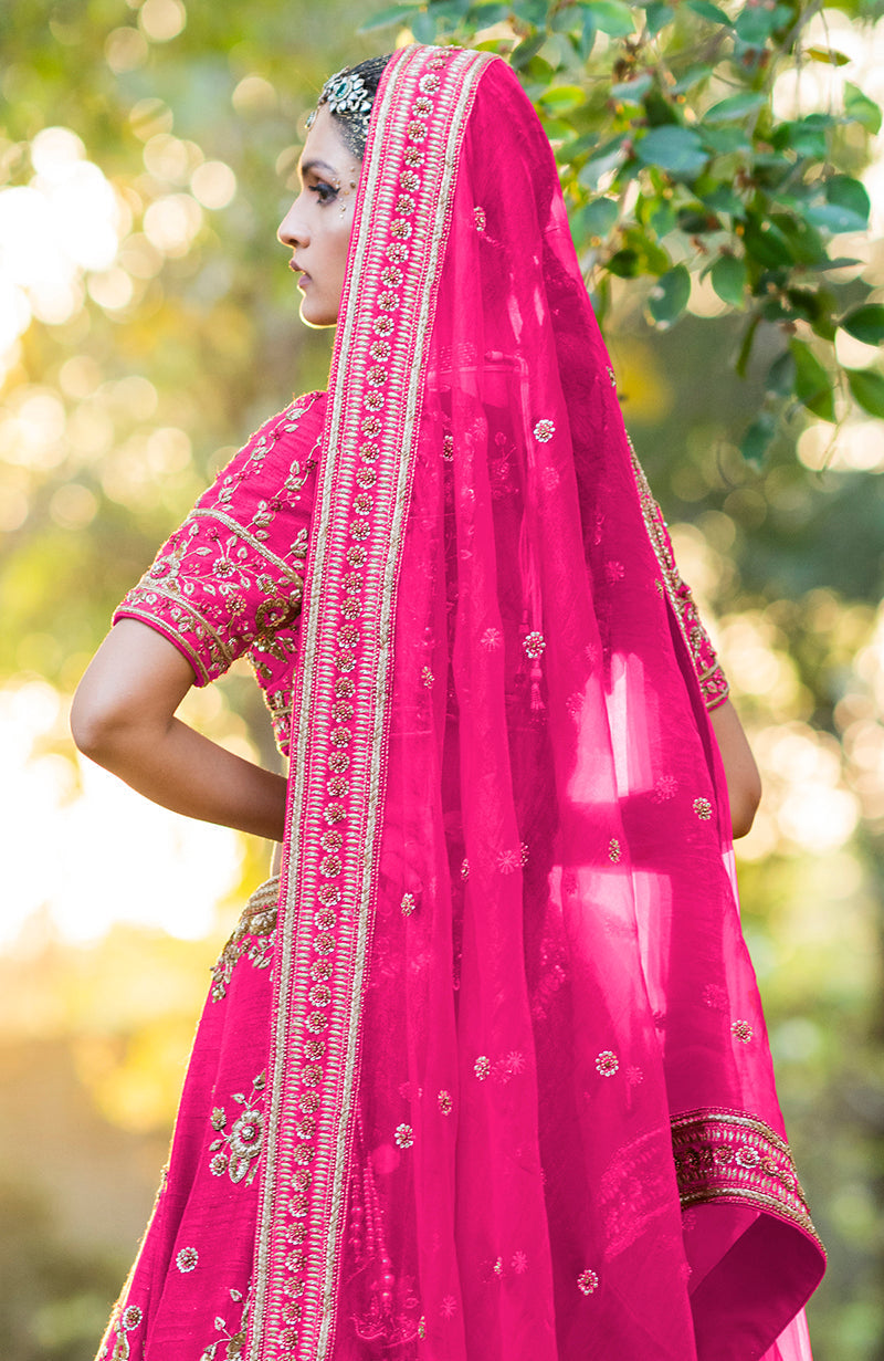 A woman in a hot pink lehenga set with gold embroidery and a sheer dupatta.