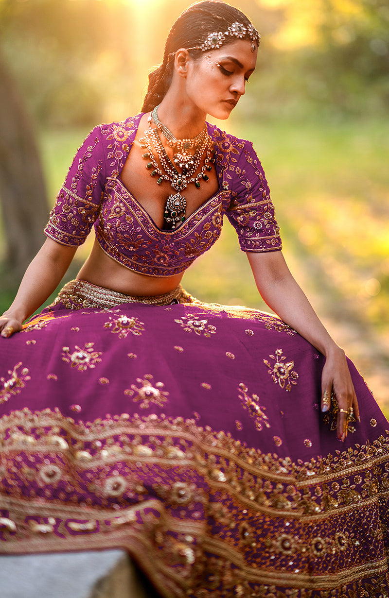 A woman models a hot pink lehenga set with gold embroidery and layered necklaces.