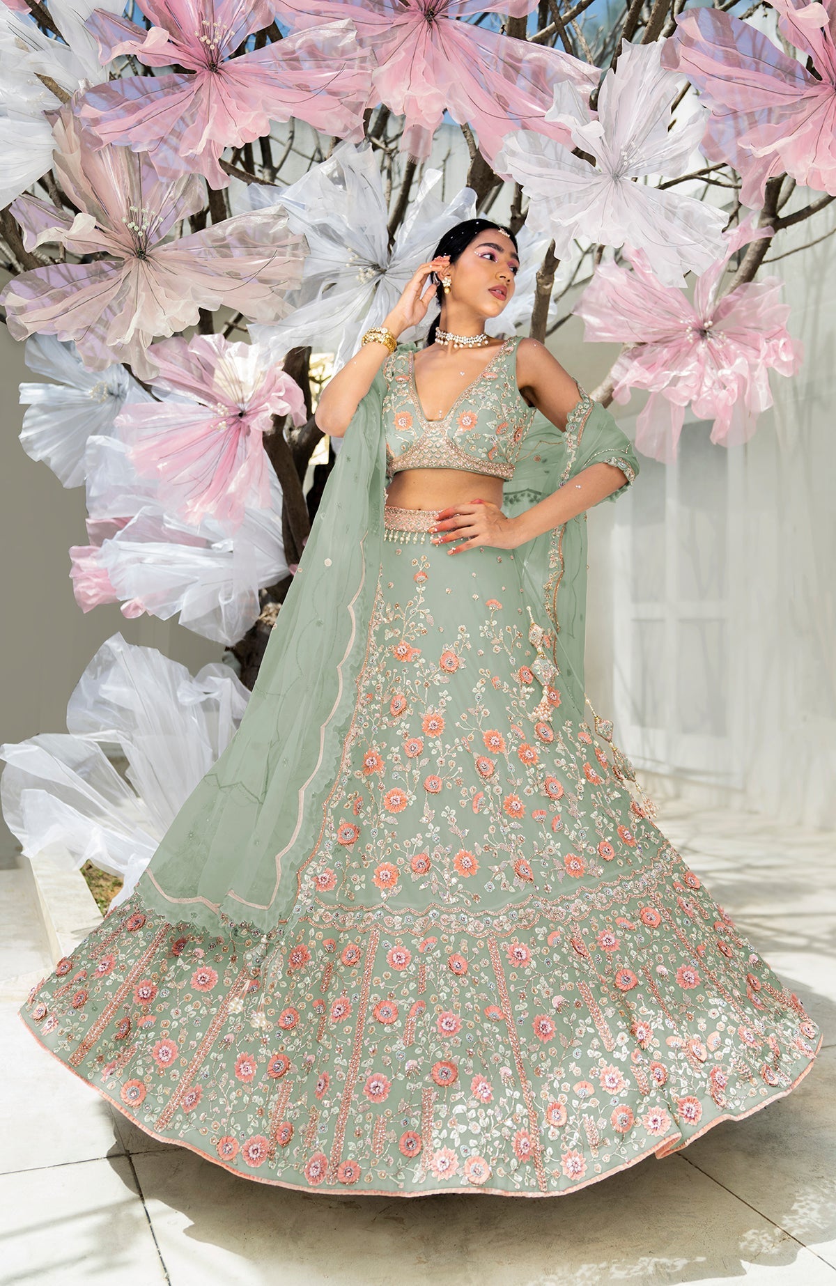A woman models a sage green lehenga set with intricate floral embroidery.