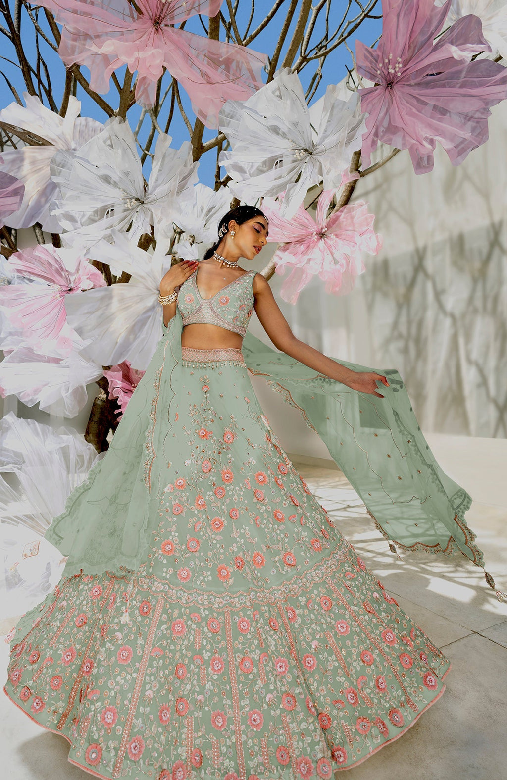 A woman models a sage green lehenga set with pink floral embroidery.