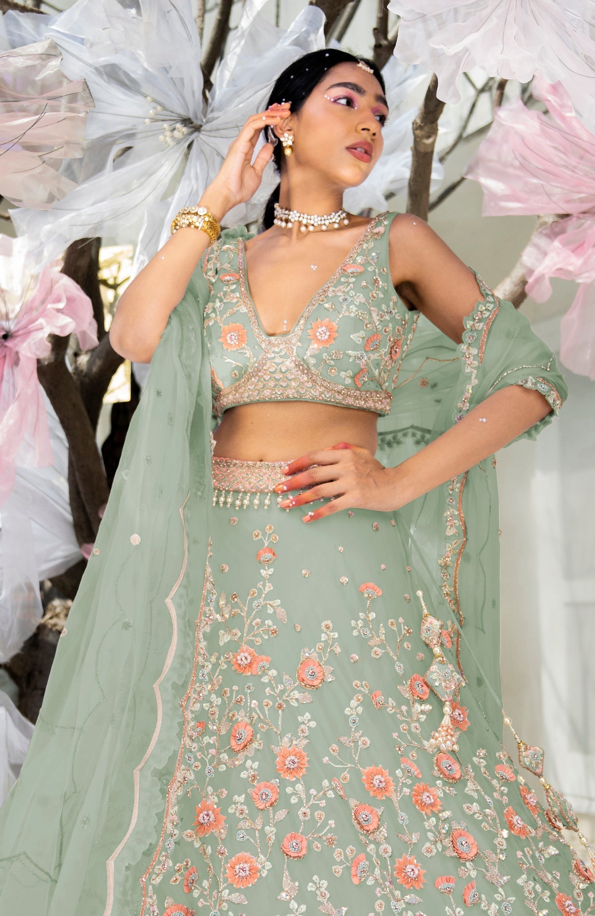 A woman models a sage green lehenga set with floral embroidery.