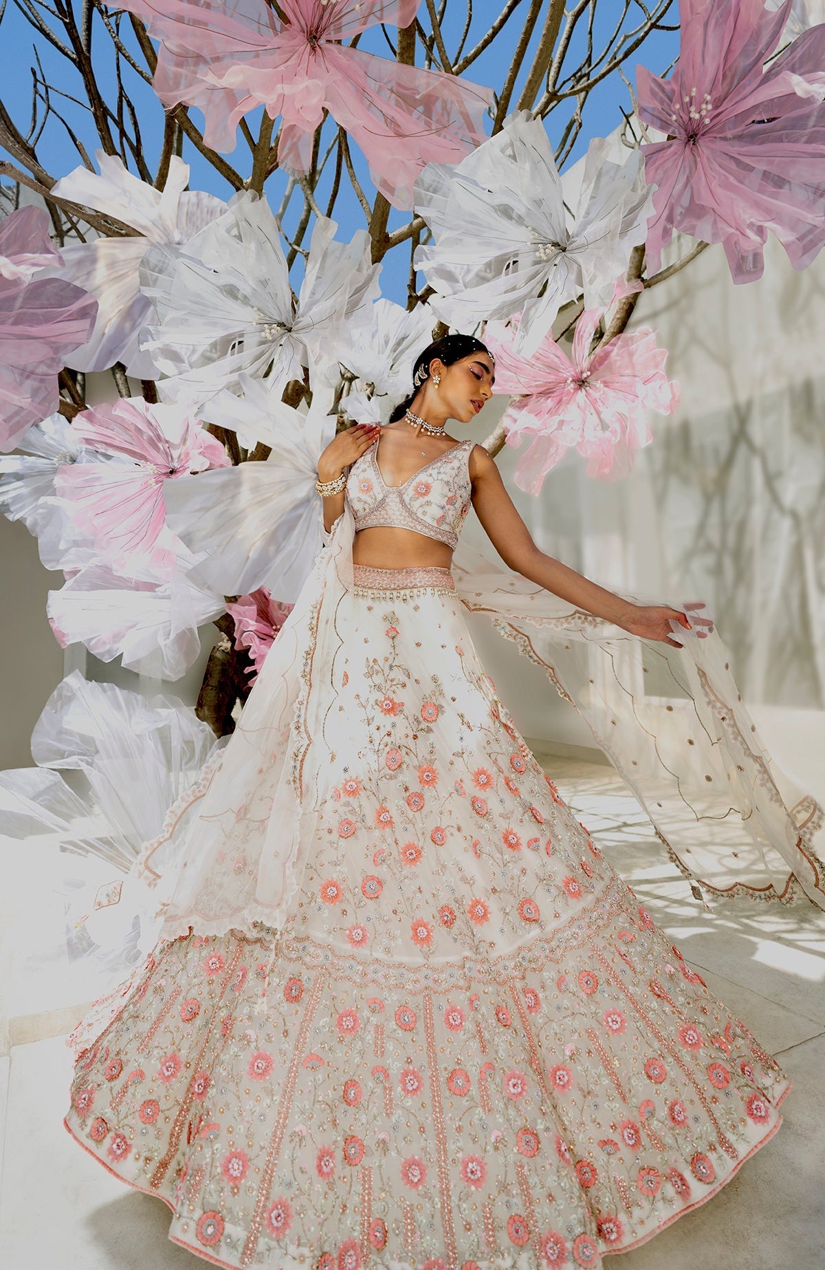 A woman models a white lehenga set with pink floral embroidery.