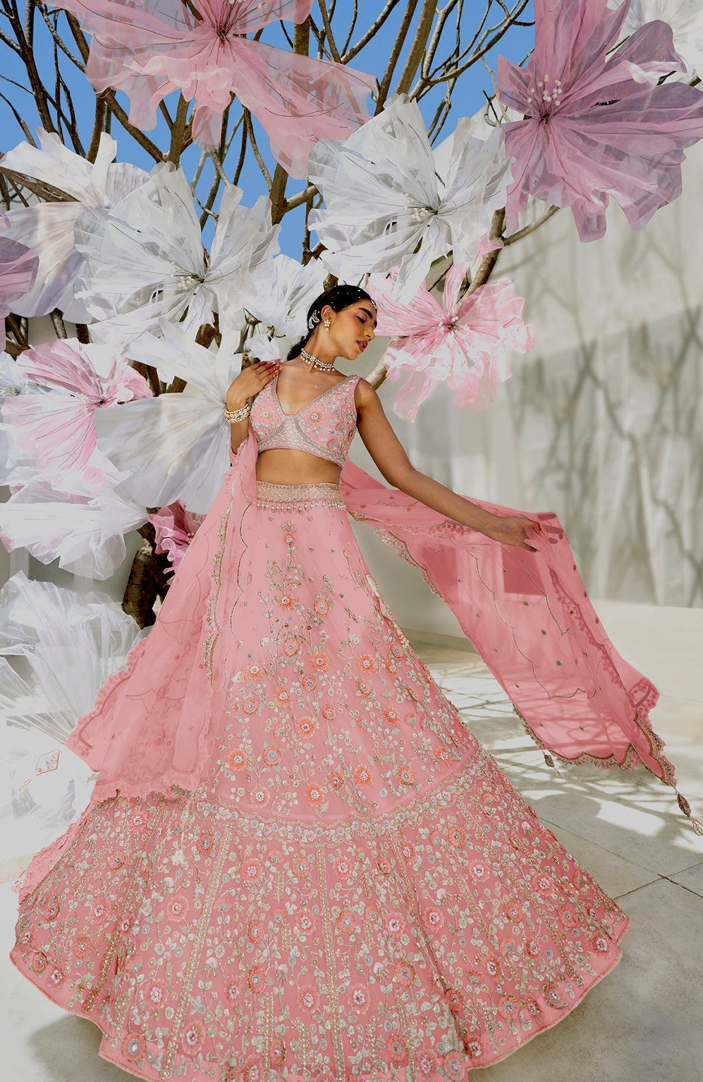 A woman models a pink lehenga set with intricate floral embroidery.