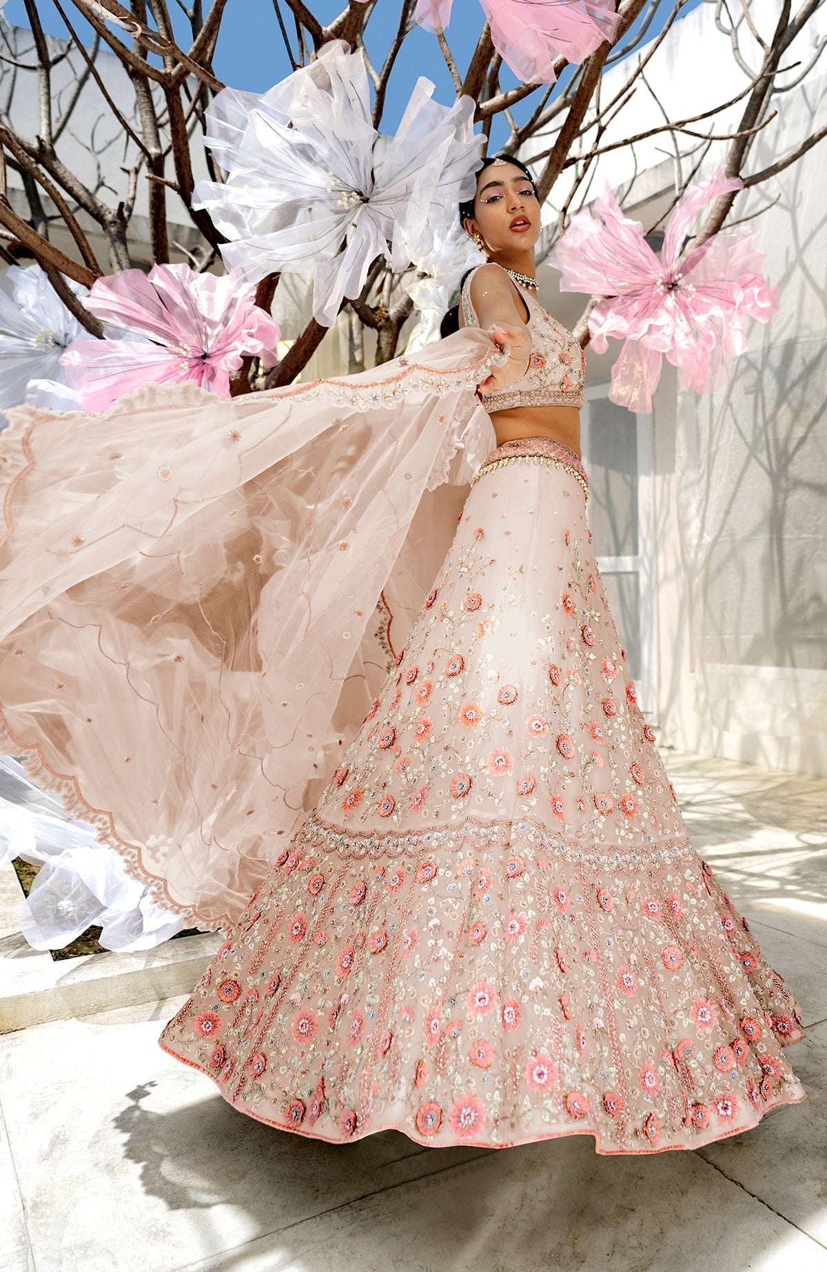 A model poses in a light pink lehenga set with floral embroidery and a sheer dupatta.