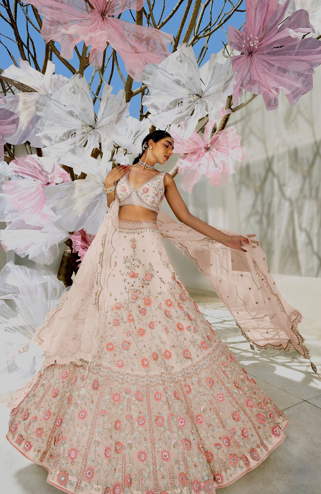 A woman models a shell beige lehenga set with intricate floral embroidery.
