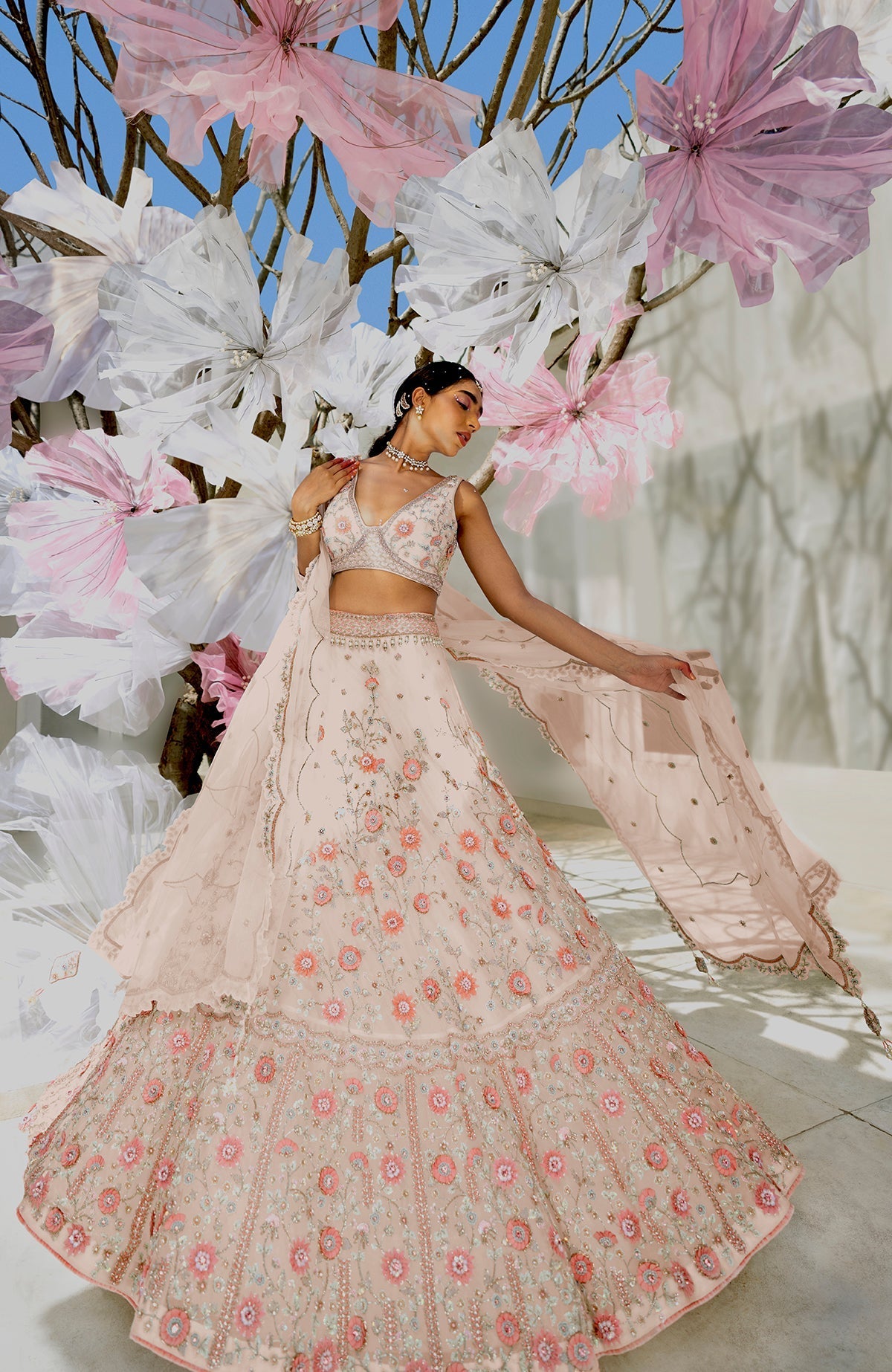 A woman models a shell beige lehenga set with intricate floral embroidery.