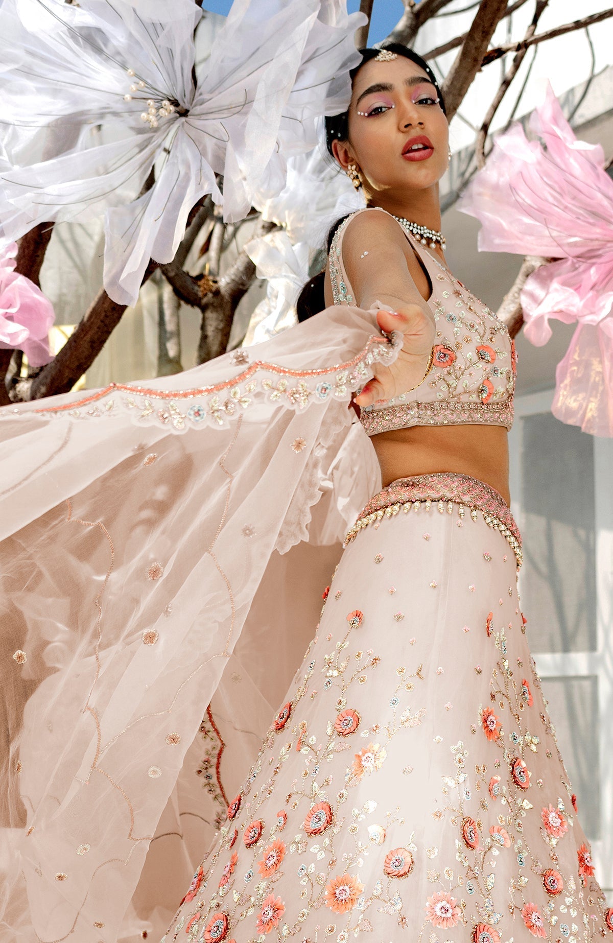 A model poses in a shell beige lehenga set with floral embroidery and a sheer dupatta.