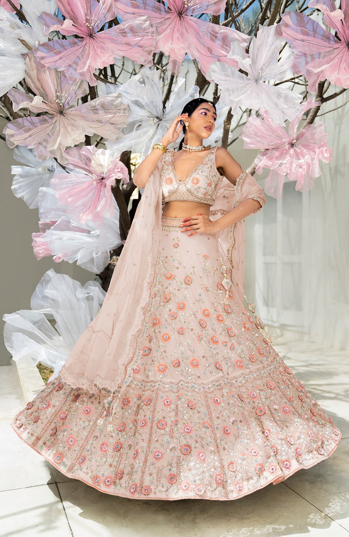 A model poses in a shell beige lehenga set with intricate floral embroidery.