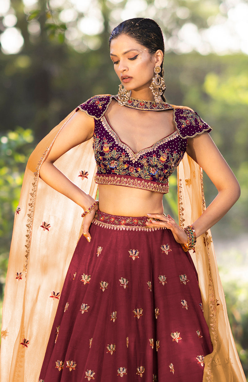 A model wears a brick red and aubergine zardozi lehenga set with a sheer dupatta.