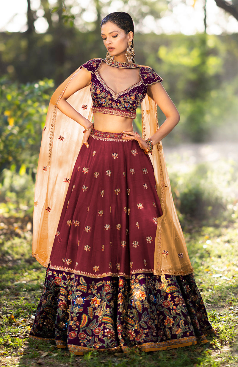 A model wears a brick red and aubergine zardozi lehenga set with a sheer dupatta.
