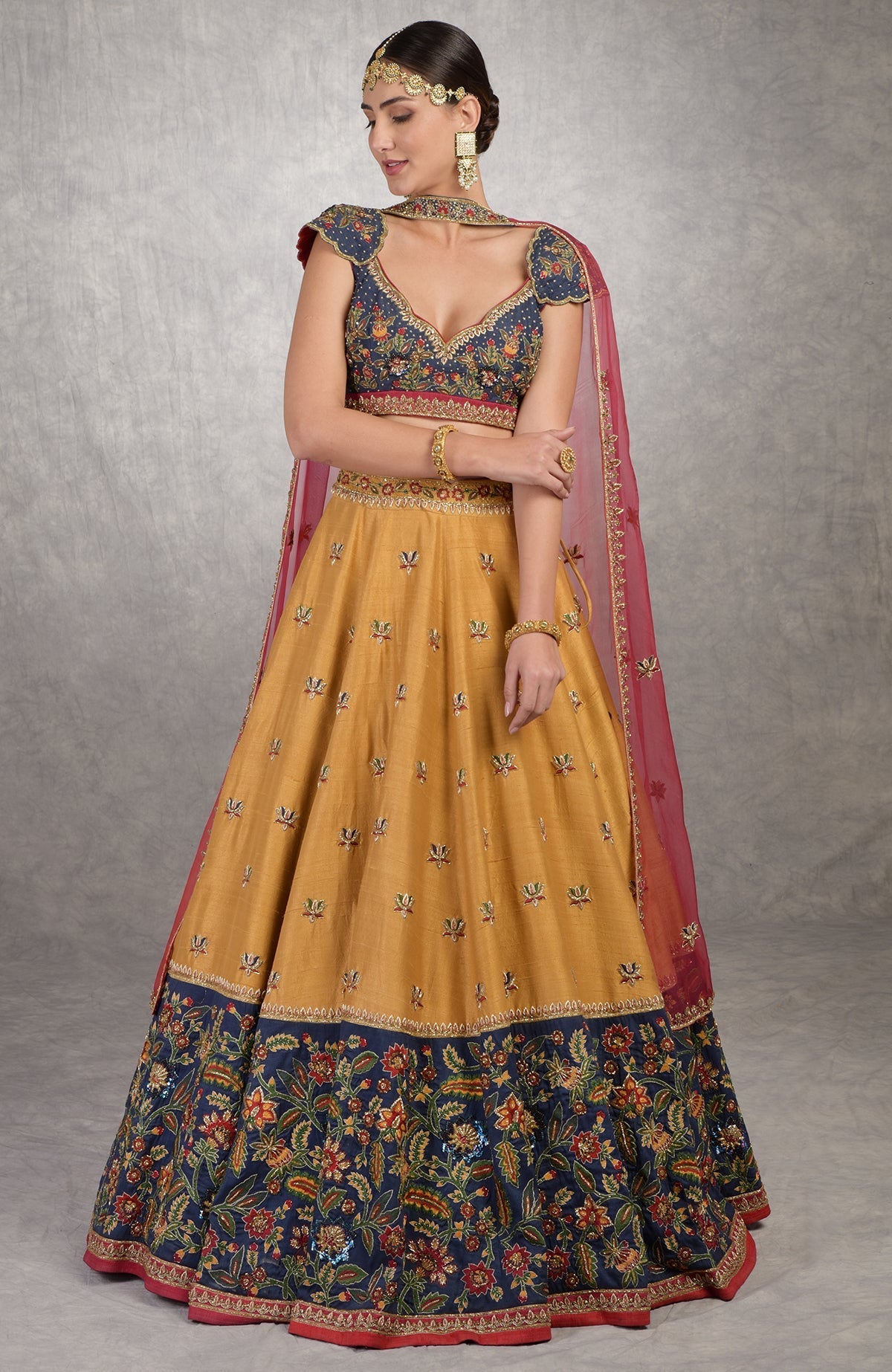 A woman models a mustard and blue lehenga with intricate floral embroidery.