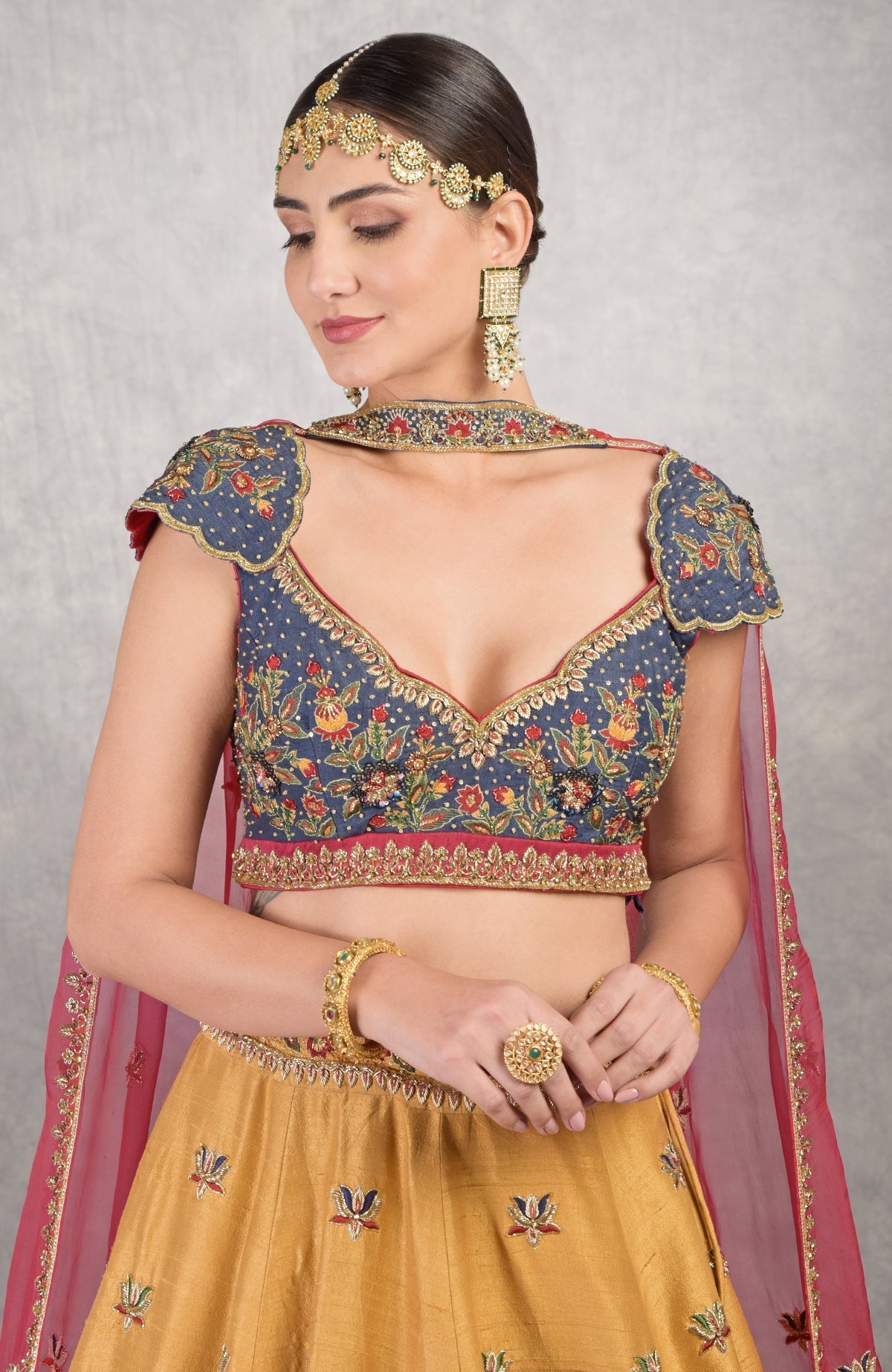 A woman in a blue embroidered lehenga with a mustard skirt and red dupatta.