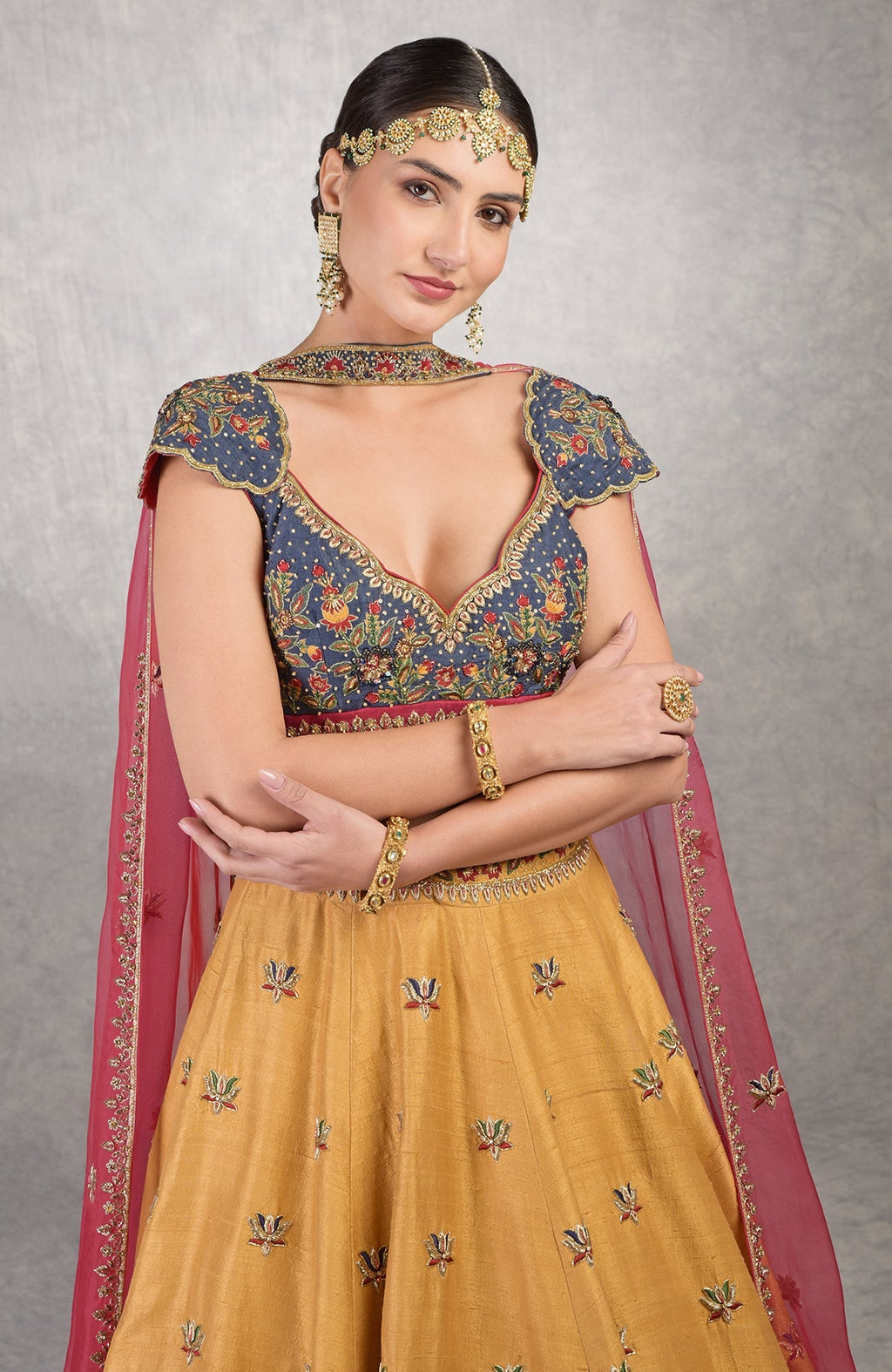 A woman models a blue embroidered blouse, mustard lehenga, and red dupatta.