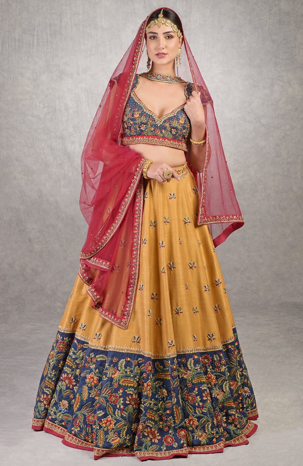 A woman models a mustard and blue lehenga with a red dupatta.