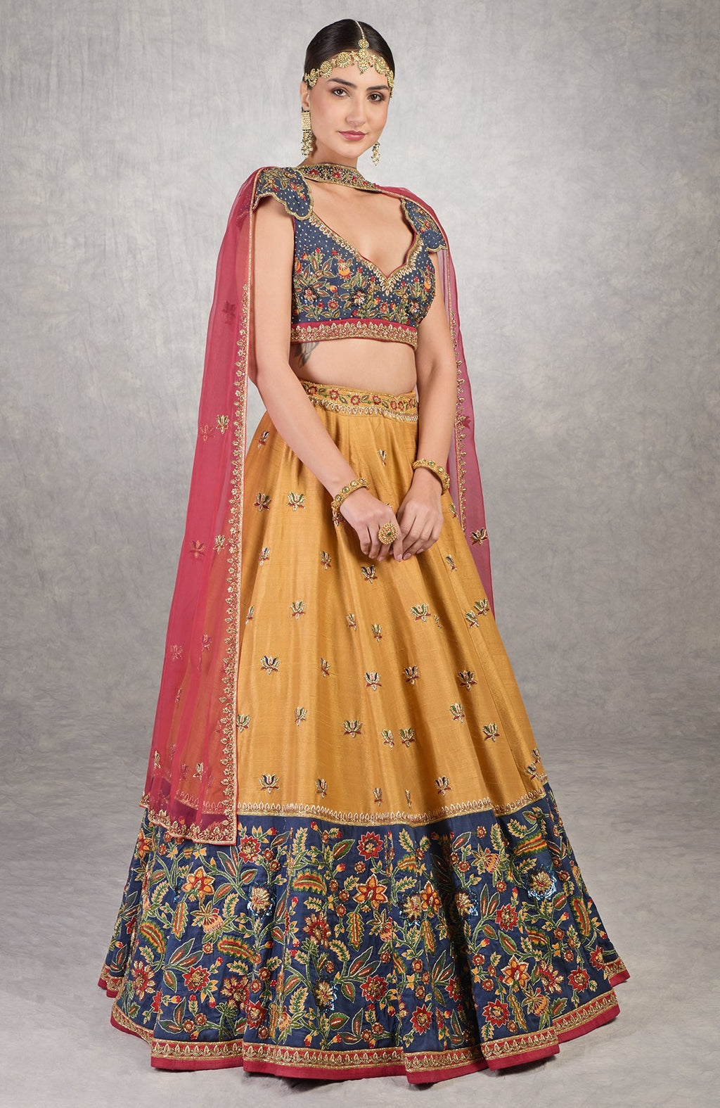 Classic blue lehenga with mustard floral embroidery, gold zardozi, and red silk organza dupatta.