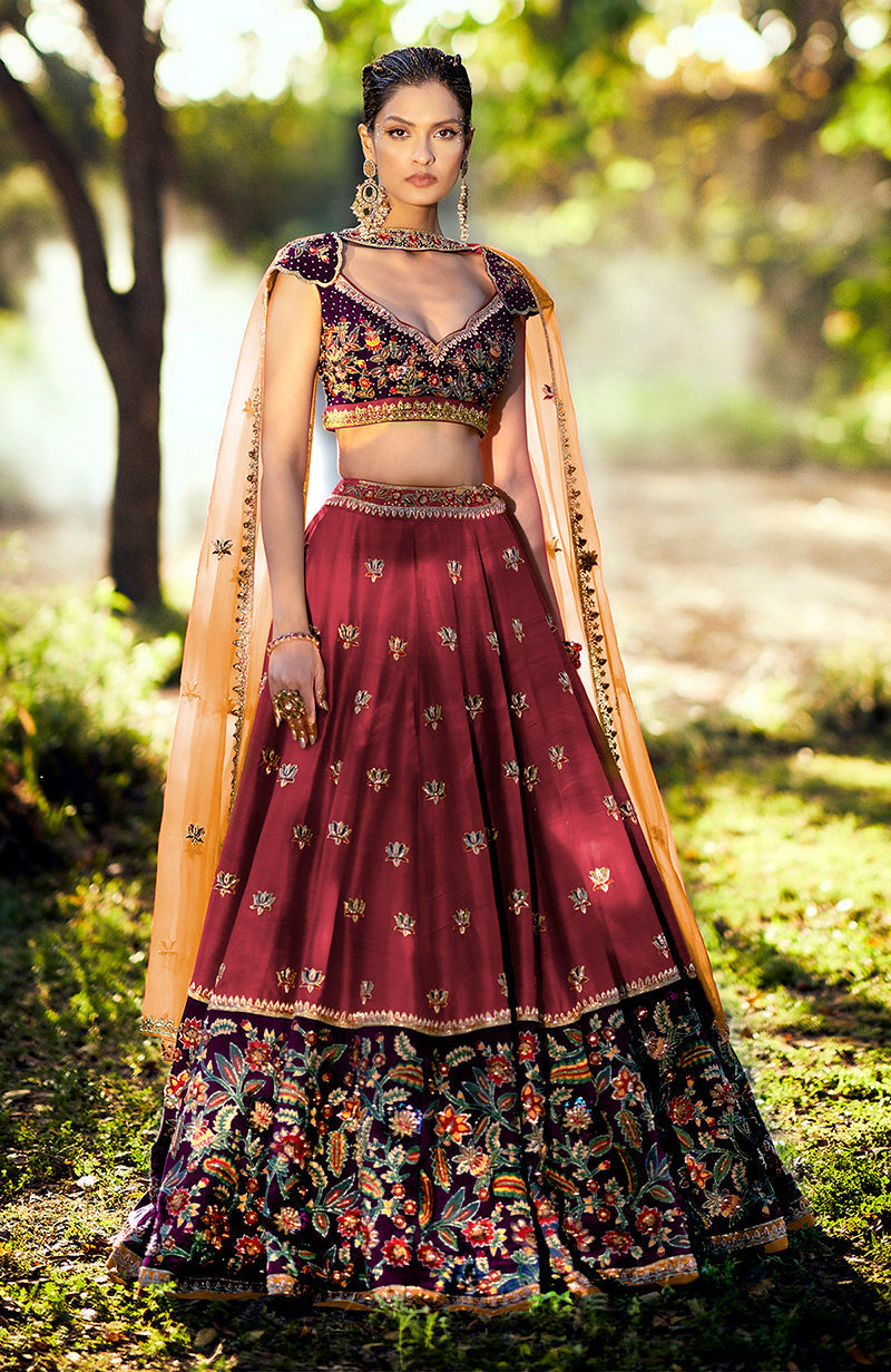 A model wears a brick red and aubergine zardozi lehenga set with an orange dupatta.